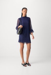 Navy blue dress with sheer bell sleeves, featuring a high neckline and ruffled accents. Paired with black open-toed mules and a mini bag.