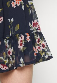 Vestido azul marino con estampado floral y dobladillo con volantes. Fabricado con una tela ligera, presenta flores rosas, rojas y verdes dispuestas de manera intrincada.