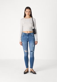 Light gray cropped long-sleeve top with a scalloped hem, paired with blue skinny jeans featuring distressed details and black flat shoes.