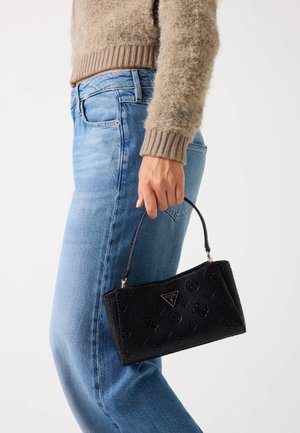Borsa a mano in finta pelle nera con motivi floreali in rilievo, manico corto e placca con logo. Indossata insieme a jeans in denim azzurro chiaro.