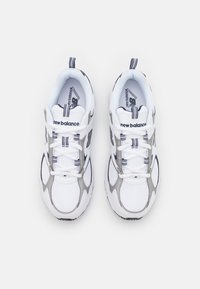 Sneakers bianchi con tomaia in rete, dettagli argentati e strisce nere sulle suole e sugli lacci. Logo "New Balance" sulla linguetta.