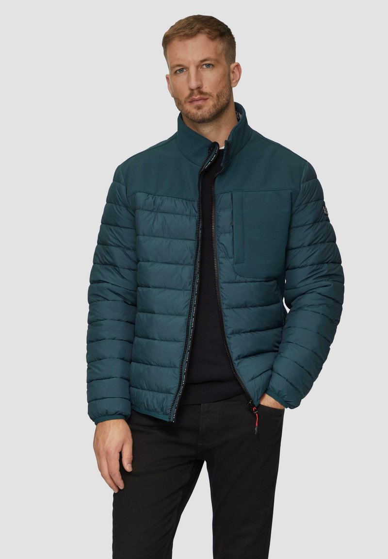 Pufferjack in diep teal, met een rits aan de voorkant, horizontale stiksels en een borstzak. De stof heeft een soepele textuur.