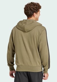 Hoodie vert olive avec un tissu texturé, doté d'une capuche et de rayures noires sur les côtés, des poignets et un ourlet côtelés, et une coupe décontractée.