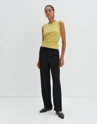 Top giallo a coste abbinato a pantaloni larghi neri e mule neri. Il top ha un collo rotondo; i pantaloni hanno una vita elasticizzata.