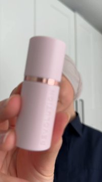 Lyst rosa beholder med matt overflate, metallisk roségullbånd, sylinderformet og med preget logo. Bakgrunnen er uskarpe kjøkkenskap.