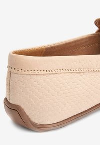 Chaussure en cuir rose clair avec motif alvéolé texturé, intérieur marron doux et semelle en caoutchouc. Arrière arrondi avec détail de couture subtil.