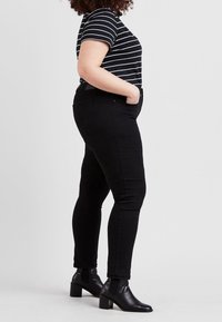 Černé skinny džíny s vysokým pasem, spárované s černobílým pruhovaným tričkem s krátkým rukávem a kotníkovými botami, ukazující štíhlou siluetu.