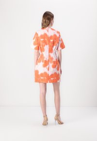 Rochie cu mâneci scurte, cu o cusătură pe spate, având un model floral portocaliu și alb pe un material neted. Este asortată cu sandale cu toc transparente.