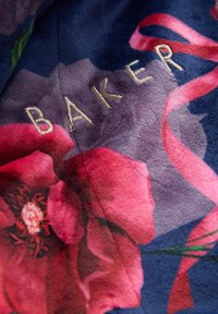 Tessuto con sfondo blu scuro, decorato da un motivo floreale rosa e con la scritta "BAKER" ricamata in oro. Texture morbida e vellutata con dettagli in raso.