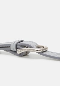 Cintura in pelle grigia chiara con hardware argentato, caratterizzata da un design ad anello e dettagli di branding incisi. Texture liscia con accenti cuciti.