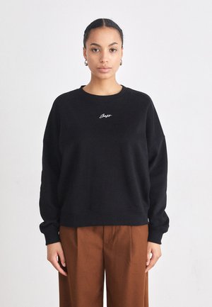Sweat-shirt noir avec un col rond et des épaules tombantes. Présente un texte brodé blanc sur la poitrine. Tissu doux, coupe décontractée, poignets côtelés.