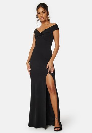 Robe noire décolletée avec un corsage ajusté, détail torsadé au niveau de la poitrine et une fente haute sur la cuisse. Tissu lisse et design longue jusqu'au sol.