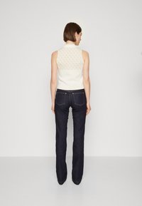 Mouwloze top in crèmekleur met een patroontas, gecombineerd met donkerblauwe flared jeans. Textuurstof, nette kraag en contrasterende kleuren zijn opgemerkt.