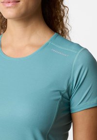 T-shirt sportivo di colore teal con superficie testurizzata, maniche corte e cuciture piatte. Logo "SWEDEMOUNT" di colore grigio chiaro lungo la spalla.