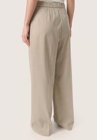Beige wide-leg bukser med elastisk taljebånd, der har en glat overflade og en baglomme, vist fra en sidevinkel.
