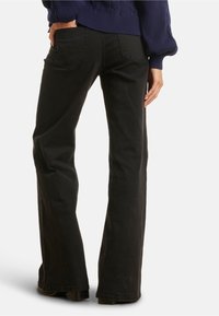 Jeans neri a palazzo con una texture liscia e due tasche posteriori, mostrati da dietro, con una leggera sfumatura e una vita strutturata.