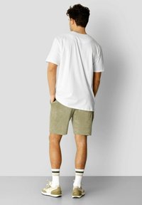 Hvit kortermet T-skjorte kombinert med lysegrønne semskede shorts. Klærne inkluderer hvite sokker med grønne striper og lyse joggesko.