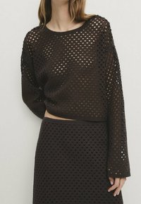 Braunes zweiteiliges Strickset mit einem kurz geschnittenen, langärmligen Oberteil mit lockerem Maschenbild und einem passenden Midirock, beide mit geometrischem Muster.