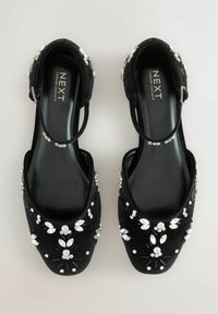 Czarne aksamitne buty o otwartym wzorze, ozdobione misternymi srebrnymi i kryształowymi detalami. W zestawie znajduje się regulowany pasek na kostkę.