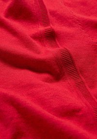 Rdeča tkanina prikazuje mehak teksturo in pletene podrobnosti, z vidnimi rebri in gladkimi raztezi, kar ustvarja brezšiven videz.