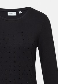 Schwarzes Langarmshirt mit Rundhalsausschnitt, das mit einer Vielzahl von strukturierten schwarzen Pailletten in einem Muster auf der Vorderseite verziert ist.
