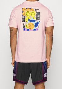 Camiseta de algodón rosa con un diseño gráfico colorido en la parte de atrás, que incluye balones de baloncesto en estilo caricaturesco, caras sonrientes y una tetera.