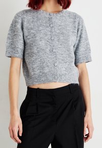 Gray short-sleeve cardigan featuring a round neckline with embellishments and button closure, paired with high-waisted black trousers.
