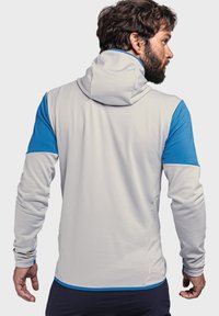 Hellegraues langärmliges Kapuzenshirt mit blauen Akzenten. Texturiertes Gewebe, taillierte Passform und Daumenlöcher an den Bündchen. Detaillierte Nähte sichtbar.