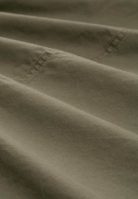 Olivenfarbener Stoff mit glatter Textur, der subtile Nähte und sanfte Falten zeigt, was auf ein leichtes Material hinweist.