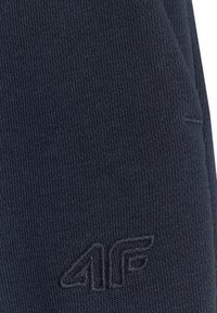 Tissu bleu foncé avec maille texturée et logo "4F" brodé en fil bleu foncé assorti près du coin inférieur droit.