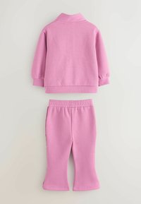 Conjunto de dos piezas rosa que incluye una blusa con cuello y mangas acampanadas, combinada con pantalones de cintura elástica con dobladillos acampanados.