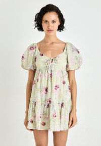Kort blommig klänning i ljusgrön tyg. Har puffärmar, fyrkantig halsringning med dragsko och en flerlagrig volangkant.