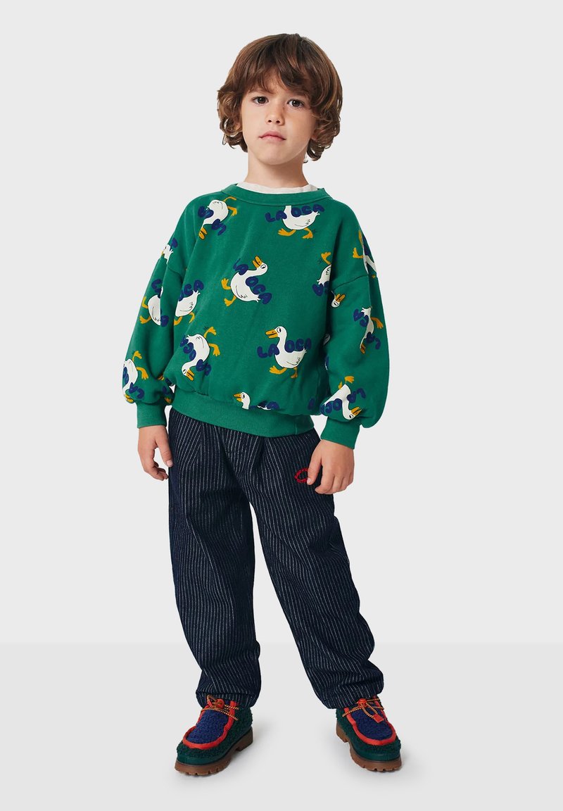 Zelená mikina s potlačou kačice a textom, v kombinácii s tmavými pruhovanými nohavicami a farebnými, textúrovanými topánkami so šnúrkami. Neformálny detský outfit.