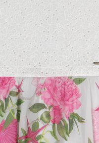 Tissu blanc avec un motif floral découpé en haut, se transformant en un matériau blanc lisse présentant de grandes pivoine roses et des feuilles vertes en bas.