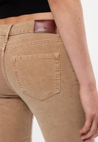 Beige corduroy broek met verticale ribbing, een achterzak en een leren label in bruin met "Pepe Jeans" merk.