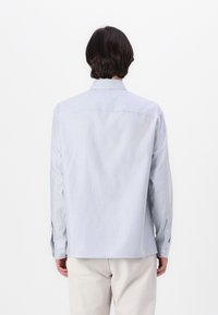 Camisa de manga larga a rayas azul claro y blanca con cuello abotonado, que presenta un yugo trasero y un dobladillo curvado. Tejido de algodón, ajuste holgado.