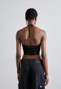 Čierny halter crop top vyrobený z saténu, s viazaním na krku a zberaným chrbtom. V kombinácii s vysokými čiernymi cargo nohavicami s logom.