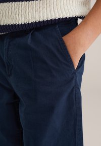 Námornícky modré bavlnené nohavice s hladkou textúrou, s bočnými vreckami a štíhlym strihom. Pás je bez ozdôb a jednoduchý.