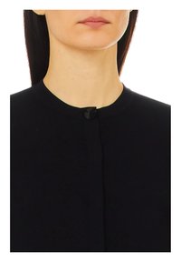 Cardigan nero in maglia con scollatura tonda, caratterizzato da una piccola chiusura con bottone nero frontale. Texture liscia, design casual.