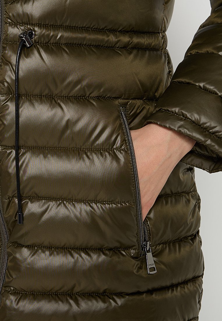 Chaqueta acolchada de color verde oliva con acolchado horizontal, un bolsillo lateral con cremallera y un cordón negro en el cuello. Textura de tela brillante.