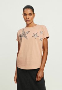 Lyserød t-shirt med korte ærmer, der har applikationer af glitrende stjerner i forskellige størrelser. Blødt bomuldsstof med en afslappet pasform.