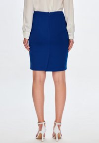 Blå strukturerad pennkjol med bakslits, dragkedjestängning och knä-längd design, ihop med vita klacksandaler.