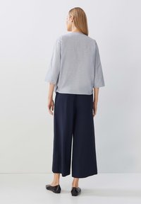 Top grigio chiaro a maniche tre quarti con una vestibilità rilassata, abbinato a pantaloni larghi blu navy. Scarpe basse nere completano l'outfit.