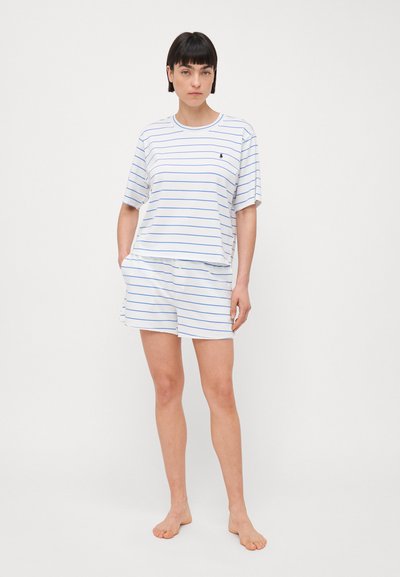 Witte katoenen T-shirt en short set, met blauwe horizontale strepen. Het T-shirt heeft een relaxte pasvorm; de shorts zijn tot halverwege de dijen en hebben een elastische tailleband.