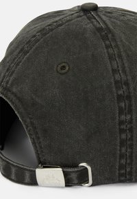 Sort denimcap med buet skygge, justerbar rem med sølvmetal hardware og en syet detalje langs sømmen.