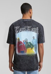 Black oversized t-shirt featuring a faded graphic print of individuals in colorful hoodies. Front reads "Karl Kani" in bold, white lettering.