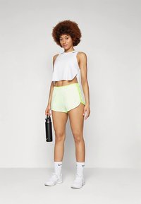 Top cropped branco, calções verdes néon com detalhes laterais, garrafa de água preta, meias brancas e sapatilhas desportivas brancas.