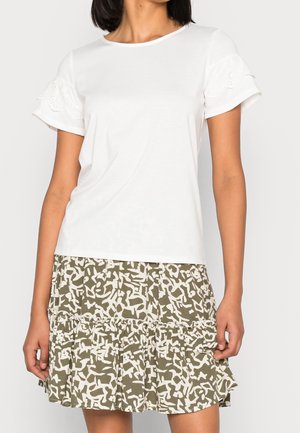 T-shirt bianca in cotone con maniche arricciate ricamate, abbinata a una gonna a strati con un motivo astratto verde e bianco.