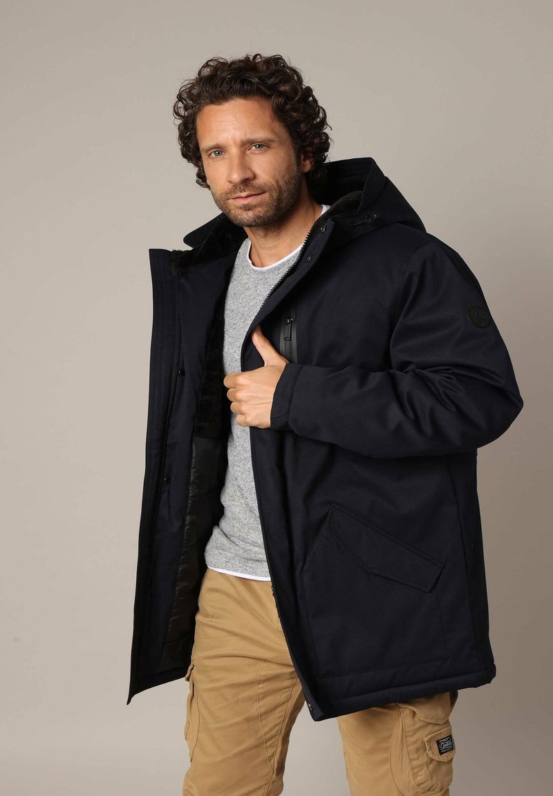 Marine parka met een capuchon, gemaakt van duurzaam materiaal. Voorzien van een ritszak en een patchzak, gevoerde binnenzijde en verstelbare sluitingen.