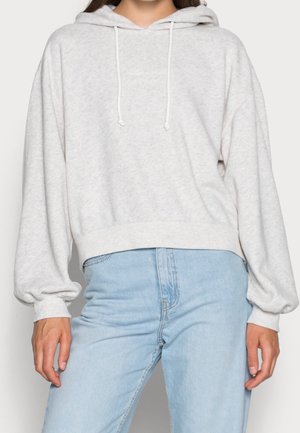 Sweat à capuche gris clair avec cordons porté avec un jean taille haute bleu clair, montré des épaules aux hanches.